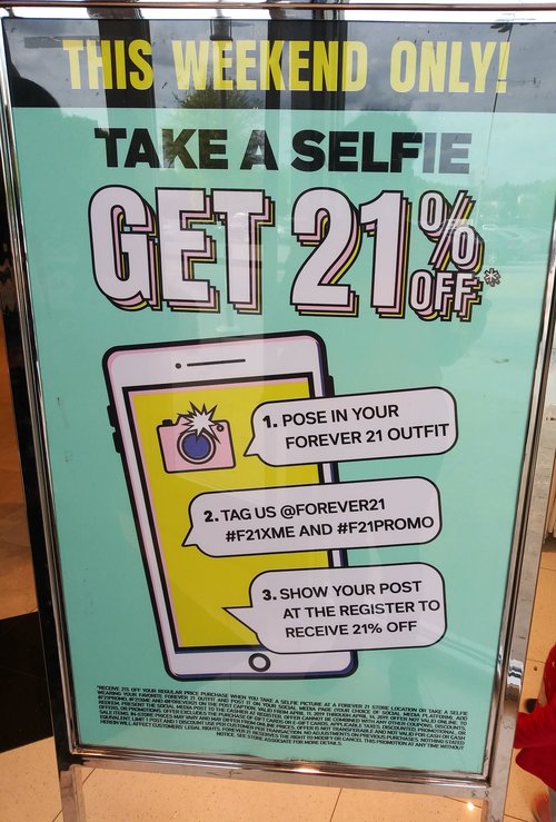 green and yellow In-store sign in Forever 21 offering shoppers a 21% discount for uploading UGC on social media and tagging the brand
